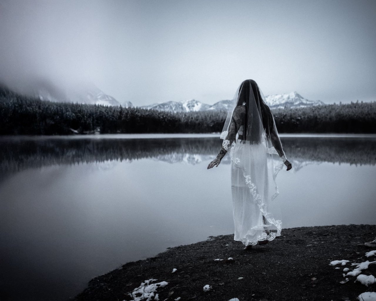 Frau im Kleid mit Schleier am winterlichen Bergsee